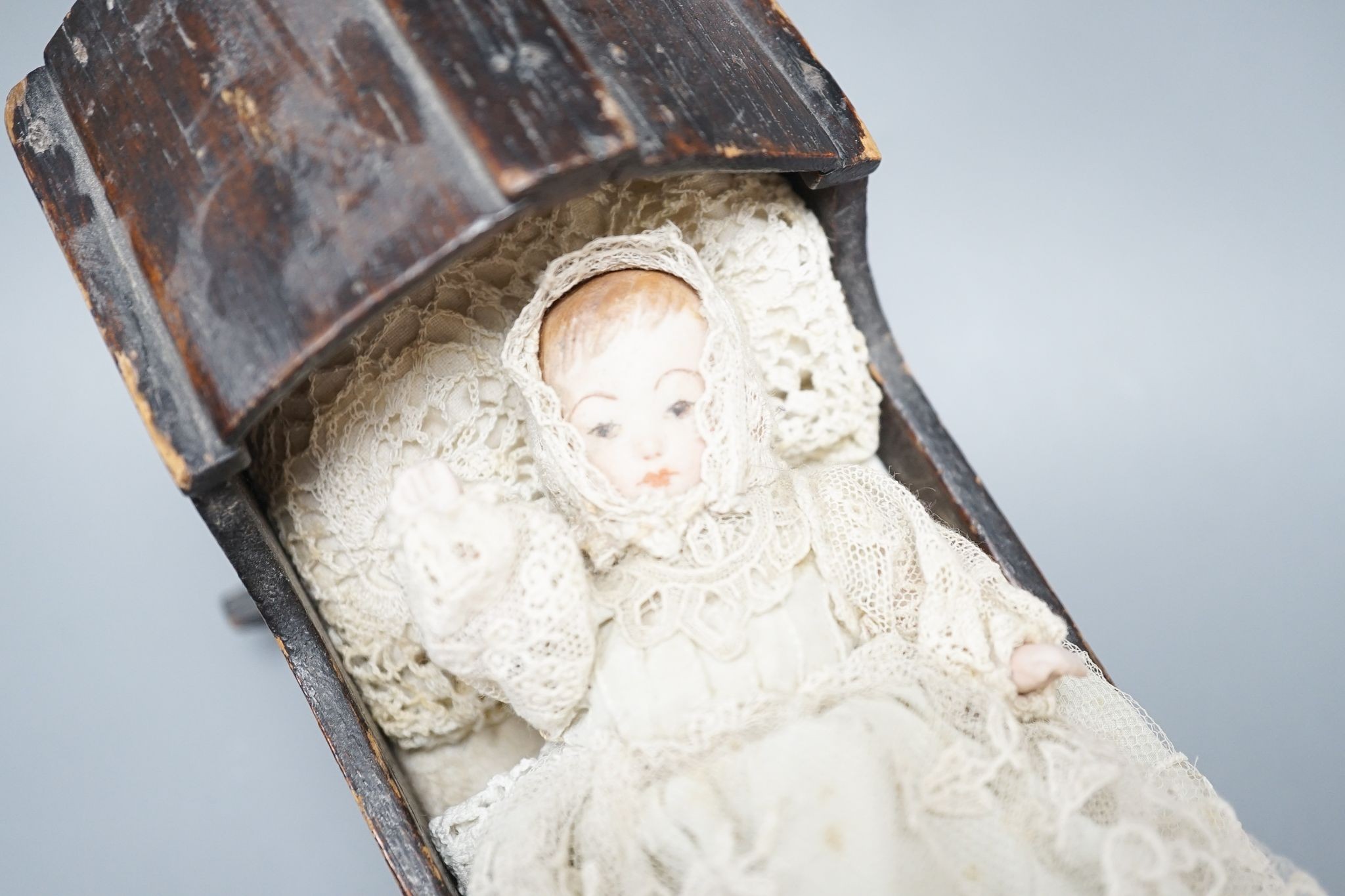 A collection of miniature bisque dolls and another larger doll in a wooden cradle, 11 dolls in total., Cradle 23.5 cms long.